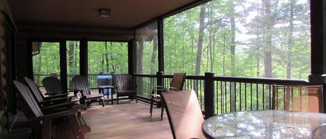 Un espace extérieur abrité doté d’un plancher en bois, d’une table en verre et de plusieurs fauteuils Adirondack.