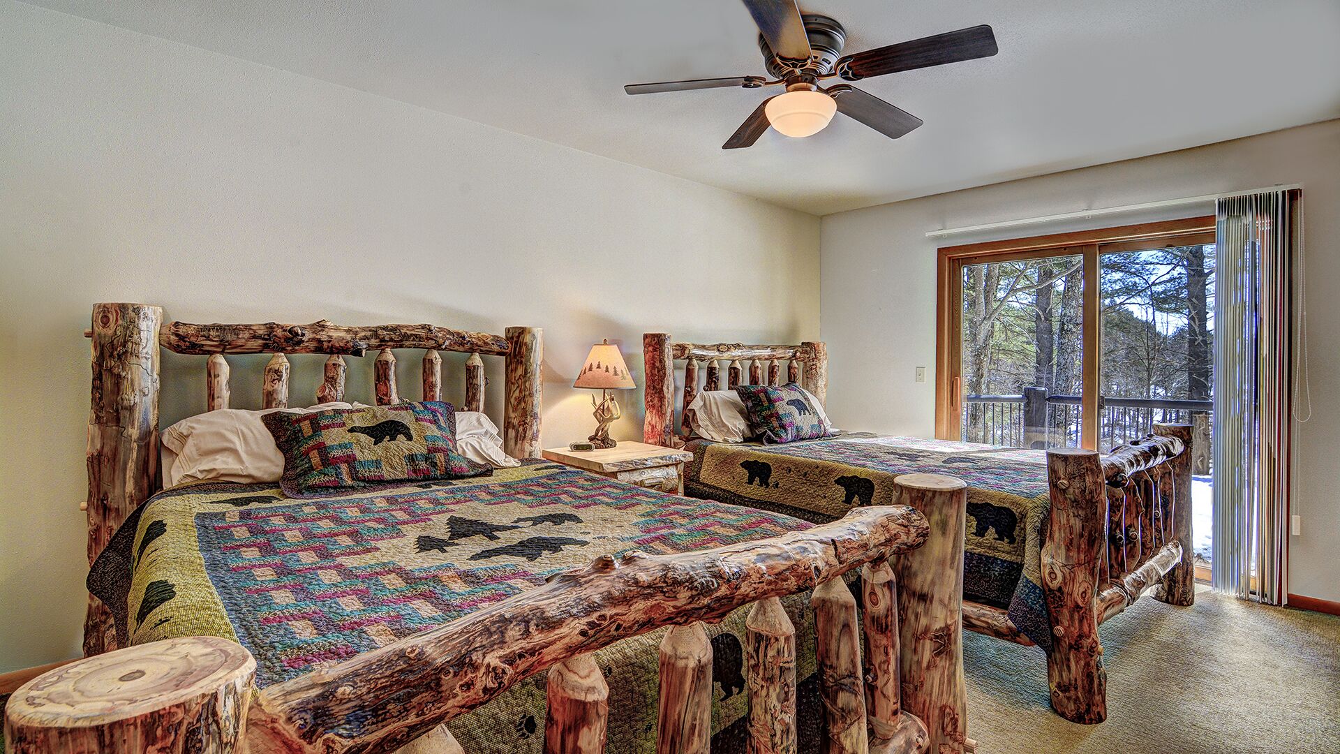A rustic bedroom with a large bed featuring a wooden headboard, a smaller bed, and a ceiling fan.