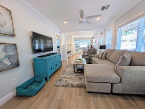 Ein geräumiges Wohnzimmer mit einem großen grauen Sofa, einem türkisfarbenen Schrank und einem flachbildfernseher an der Wand.