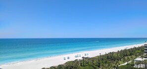 A beach with white sand, clear blue water, and a row of blue umbrellas.