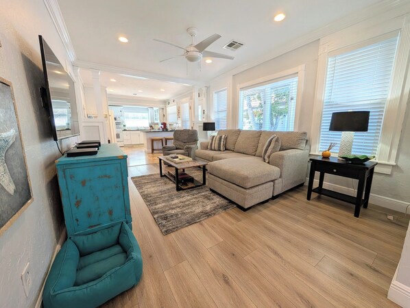 A spacious living room with a large sectional sofa, a teal armchair, a coffee table, and a TV on a stand.
