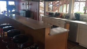 Een keuken met een bar, houten kastjes, een roestvrijstalen afzuigkap en een raam met uitzicht op de omgeving.