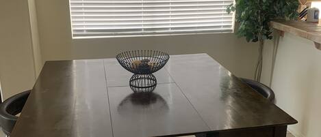 A dining table with a black wire basket in the center, flanked by two dark brown chairs.