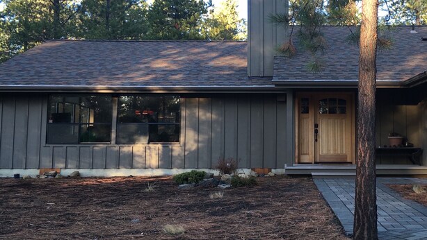 Une maison moderne avec une façade grise, une porte d’entrée en bois et un petit porche.