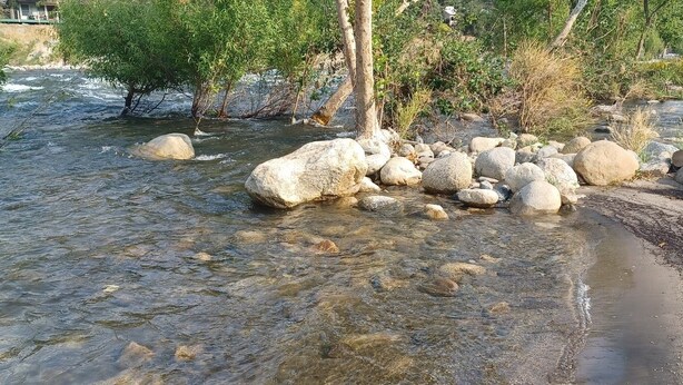 Ein Fluss mit klarem Wasser, umgeben von Felsen und Vegetation.