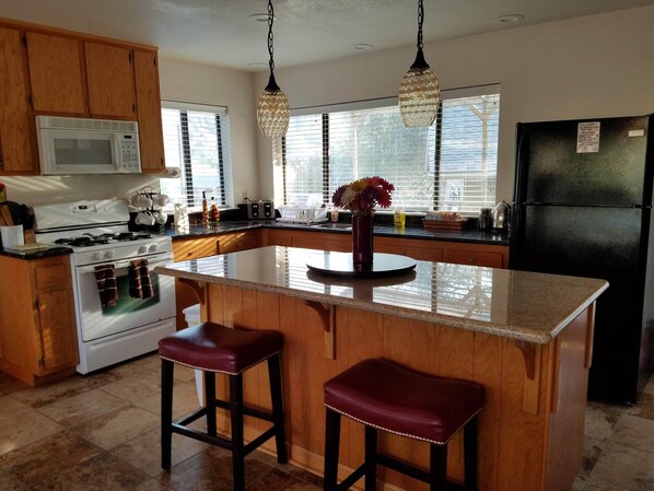A kitchen with wooden cabinets, a white stove, a black refrigerator, and a large island with two stools. - Awesome house & Kaweah River access and 5 miles to Sequoia Park (Three Rivers)