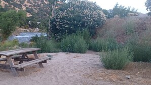 Ein Picknicktisch in einer natürlichen Umgebung, mit einem Fluss und Hügeln im Hintergrund.