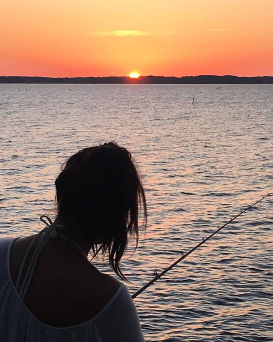 Une personne est en train de pêcher au coucher du soleil, la mer est calme et le ciel est dégagé.