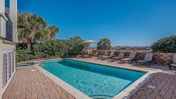 A rectangular pool with a tiled edge, surrounded by a brick patio. There are lounge chairs and a table with an umbrella. - Direct Oceanfront Luxury Home, Large Private Pool and Spa, Elevator, Concierge! (Hilton Head Island)