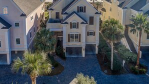 A multi-story residential building with a central entrance, surrounded by palm trees and a paved driveway. - Direct Oceanfront Luxury Home, Large Private Pool and Spa, Elevator, Concierge! (Hilton Head Island)