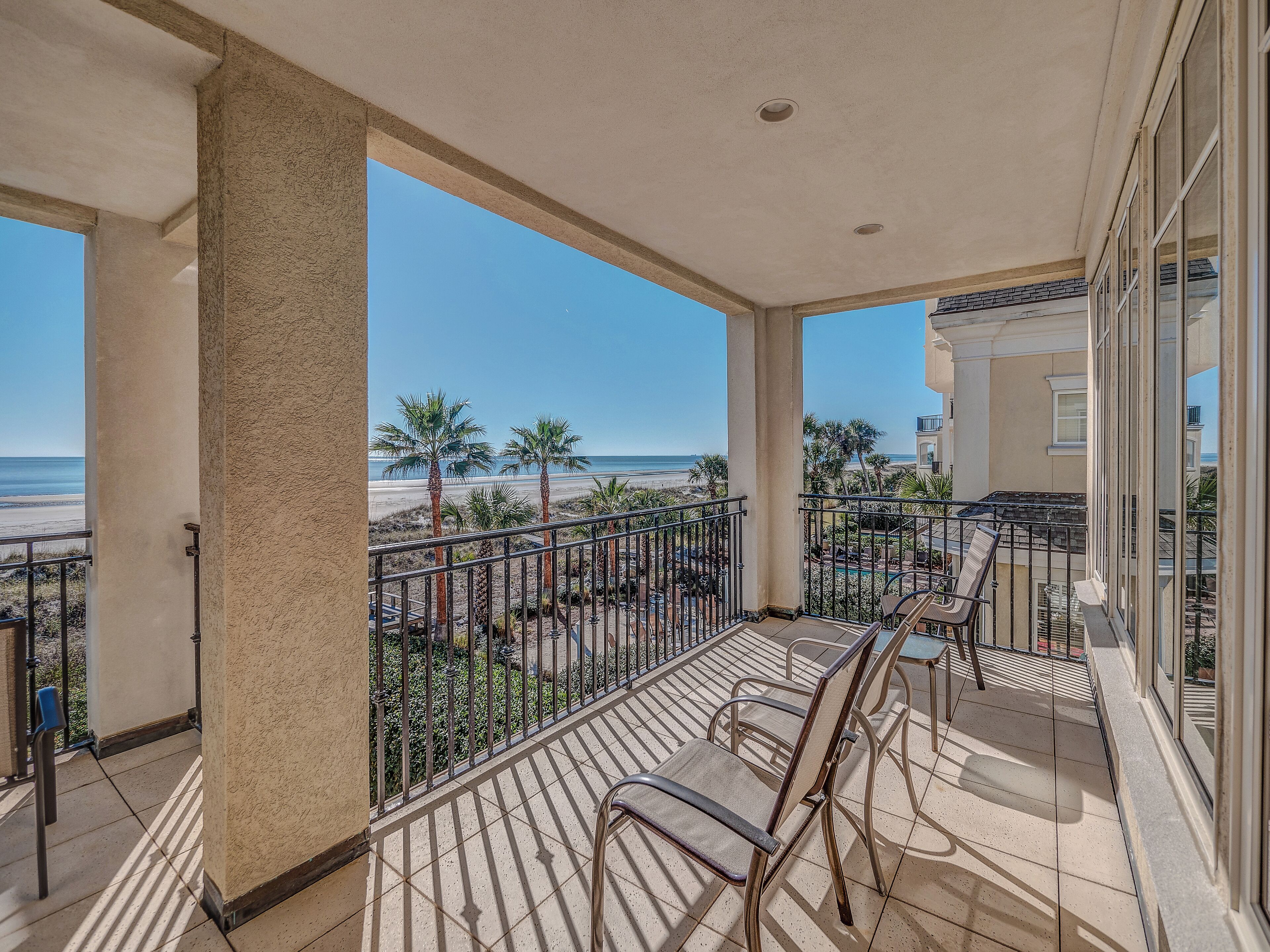 A balcony with a view of the beach, equipped with chairs and a railing.