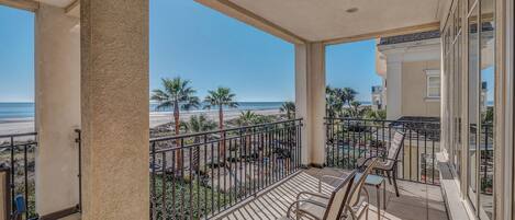 A balcony with a view of the beach, equipped with chairs and a railing.