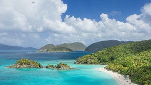 A tropical beach with clear turquoise waters, a sandy beach, and lush green hills in the background. - Grande Bay Condo Beautiful Morning- 3 Bedroom - Wraparound Balcony- Views!! (St John)