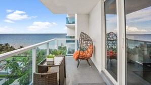 Un balcon avec une table en osier, une chaise dotée d’un coussin orange et une vue sur l’océan.