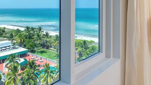 Une chambre d’hôtel dotée d’une grande fenêtre donnant sur une plage et l’océan.