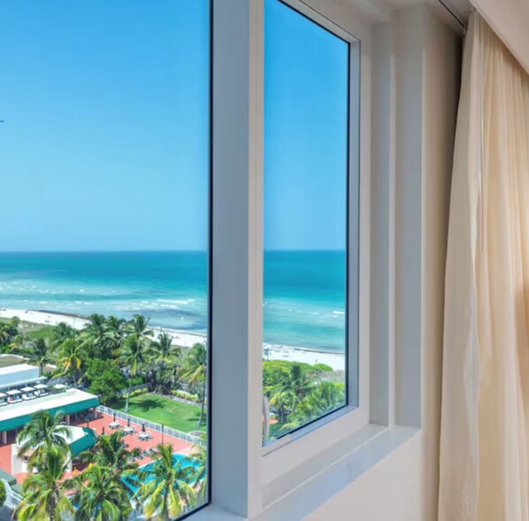 Habitación de hotel con un amplio ventanal con vistas a una playa y al océano.