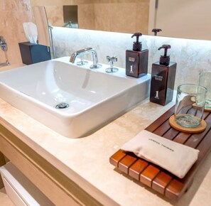 Une salle de bain moderne avec un grand lavabo blanc, plusieurs robinets et un distributeur de savon en verre.