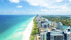 Un paysage urbain côtier avec de hauts immeubles le long d’une plage, un ciel bleu dégagé et une vue sur l’océan.