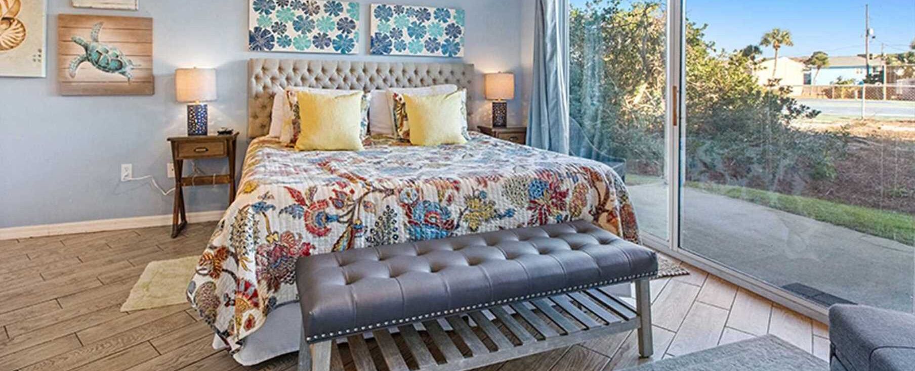A bedroom with a large bed, a bench, and a view of the outdoors.