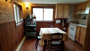 Eine kleine Küche mit Holzschränken, einem Esstisch mit Stühlen, einem eingebauten Backofen und einer Kaffeemaschine.