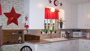 A kitchen with white cabinets, a red star decoration, a clock, and a window with a red curtain.