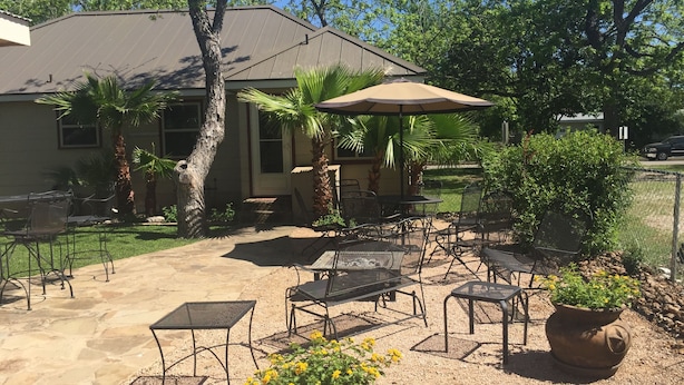 An outdoor patio with metal tables and chairs, a large umbrella, and potted plants.