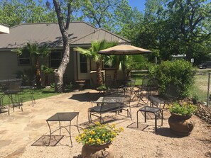 An outdoor patio with metal tables and chairs, a large umbrella, and potted plants.