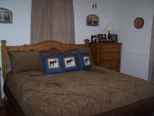 A bedroom with a wooden headboard, a bed with a brown patterned bedspread, and two pillows with animal designs.