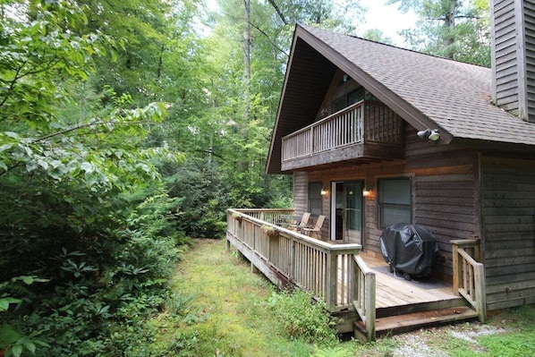 A wooden cabin with a balcony, surrounded by dense forest.