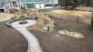 Un giardino curato con un vialetto in mattoni che si snoda, cerchi di pietra decorativi e una recinzione in legno.
