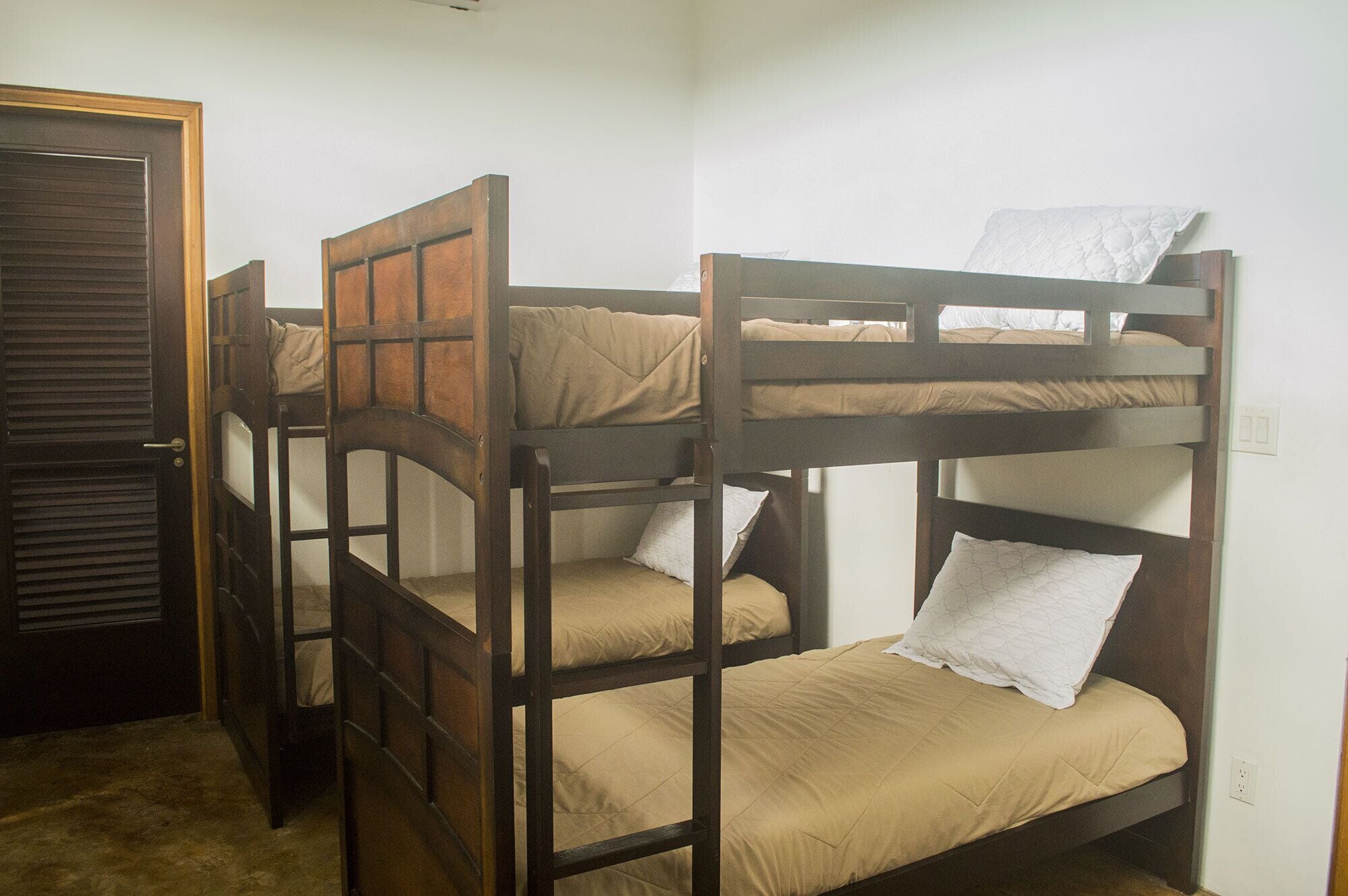 Une chambre avec un lit superposé, deux lits, une porte et un interrupteur sur le mur.