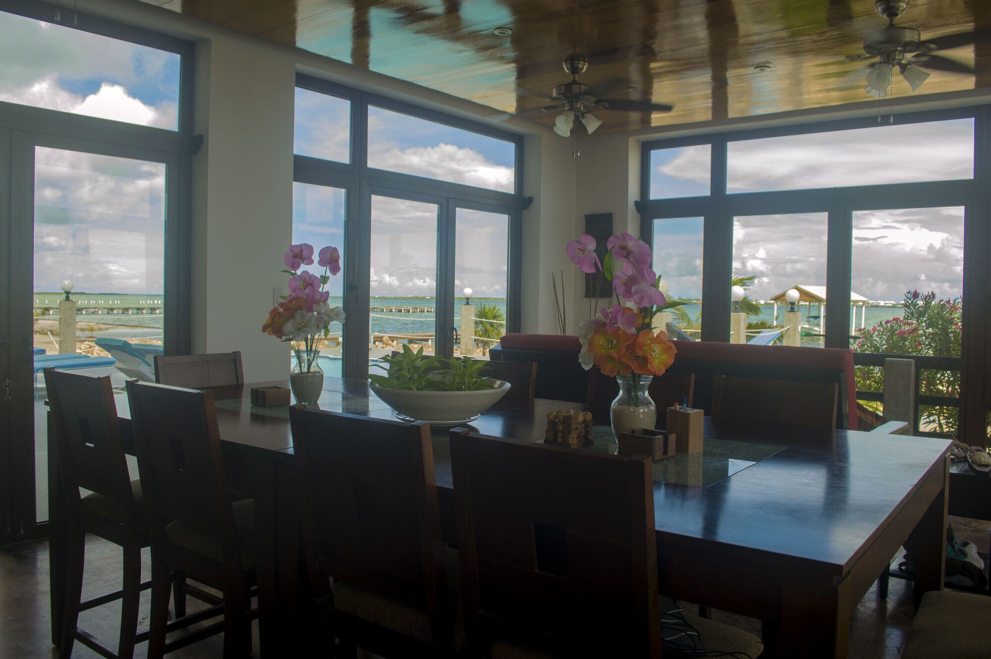 A dining area with a view of the beach, large windows, and a ceiling fan.