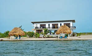 A two-story building with a balcony, a pool area with lounge chairs, and thatched umbrellas. - Seafront, 4 bedroom private villa, 10 guests, family vacation, activities nearby (Ambergris Caye)