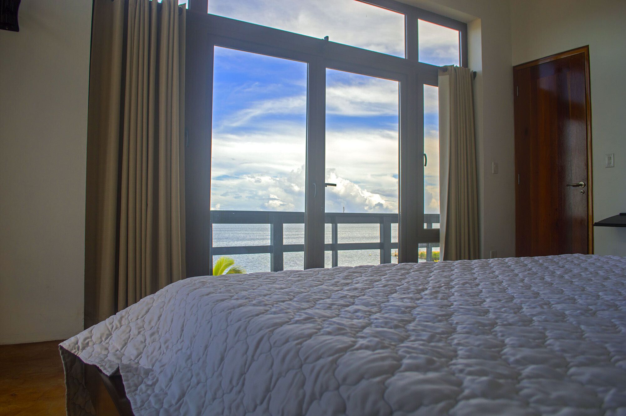 Ein Schlafzimmer mit großem Fenster, einem Bett und einer Holztür.