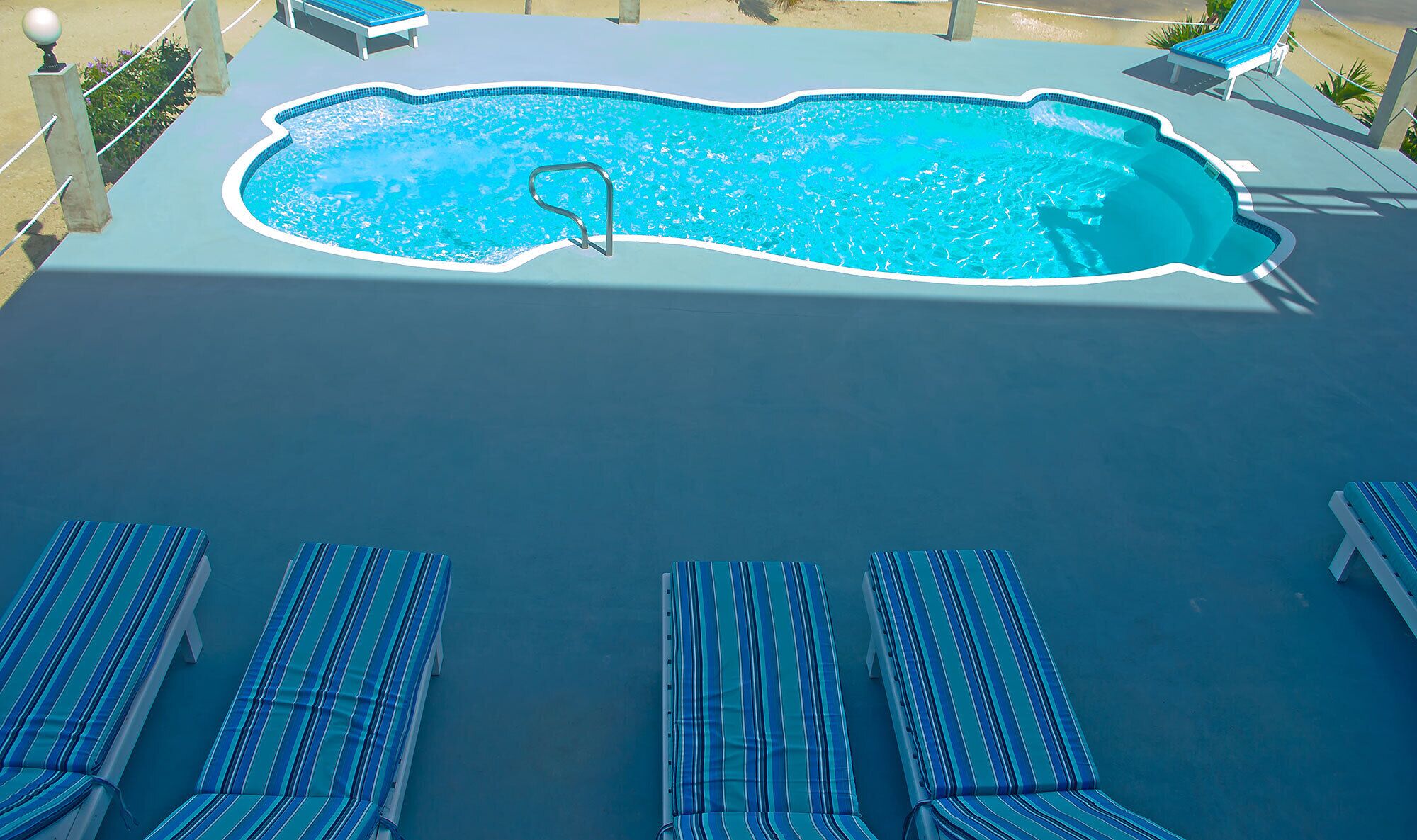 A swimming pool with a tiled edge, surrounded by lounge chairs with striped cushions.