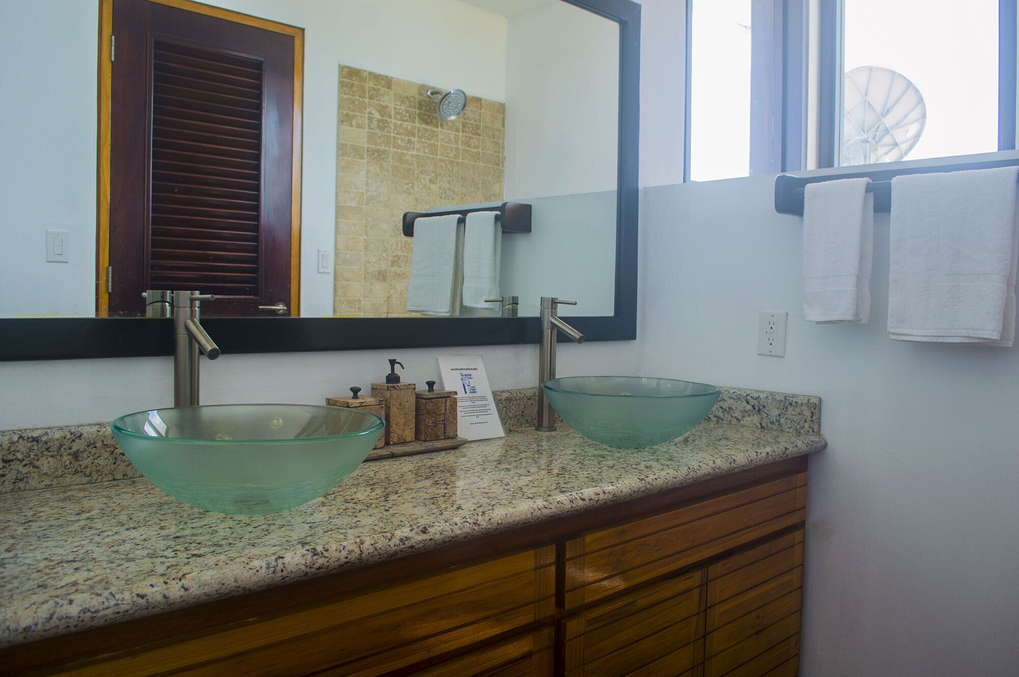 A bathroom with two glass sinks, a large mirror, and a window with a view of a windmill.