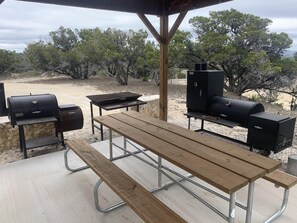 An outdoor patio with a wooden table and benches, surrounded by barbecue grills and a stone wall. - Sleeps 33, Private pool & putting green,10 min from Garner State Park, Frio Riv. (Utopia)