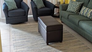 Una sala de estar con dos sillones, un sofá, una mesa de centro, un ventilador de techo y una ventana con persianas.