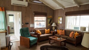 A cozy living room with wooden walls, a green armchair, a brown sofa set, and a dining table.