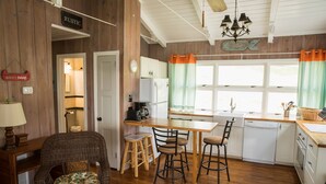 A rustic kitchen with wooden walls, a dining area with a table and chairs, and a view through the window.
