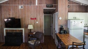 A rustic cabin interior with a TV, fireplace, dining table, chairs, and a kitchen area.