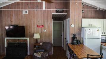 A rustic cabin interior with a TV, fireplace, dining table, chairs, and a kitchen area.