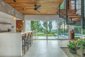 Una cocina moderna con barra, grandes puertas correderas de vidrio que dan a una piscina y techo de madera.