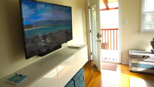 Ein Wohnzimmer mit einem Flachbildfernseher an einem weißen Schrank, einem blauen Sofa und Holzboden.