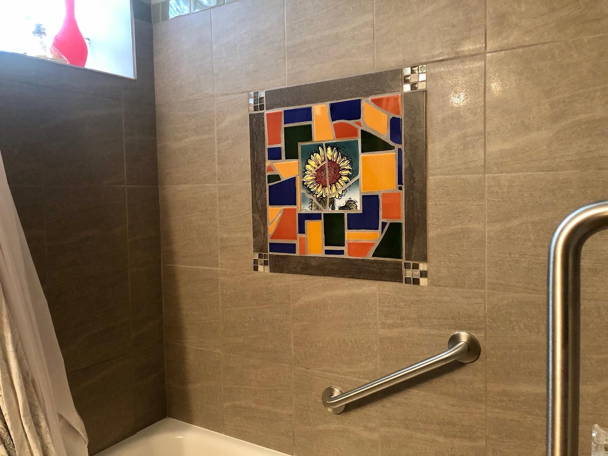 A bathroom with a tiled wall, a decorative tile piece, and a grab bar.
