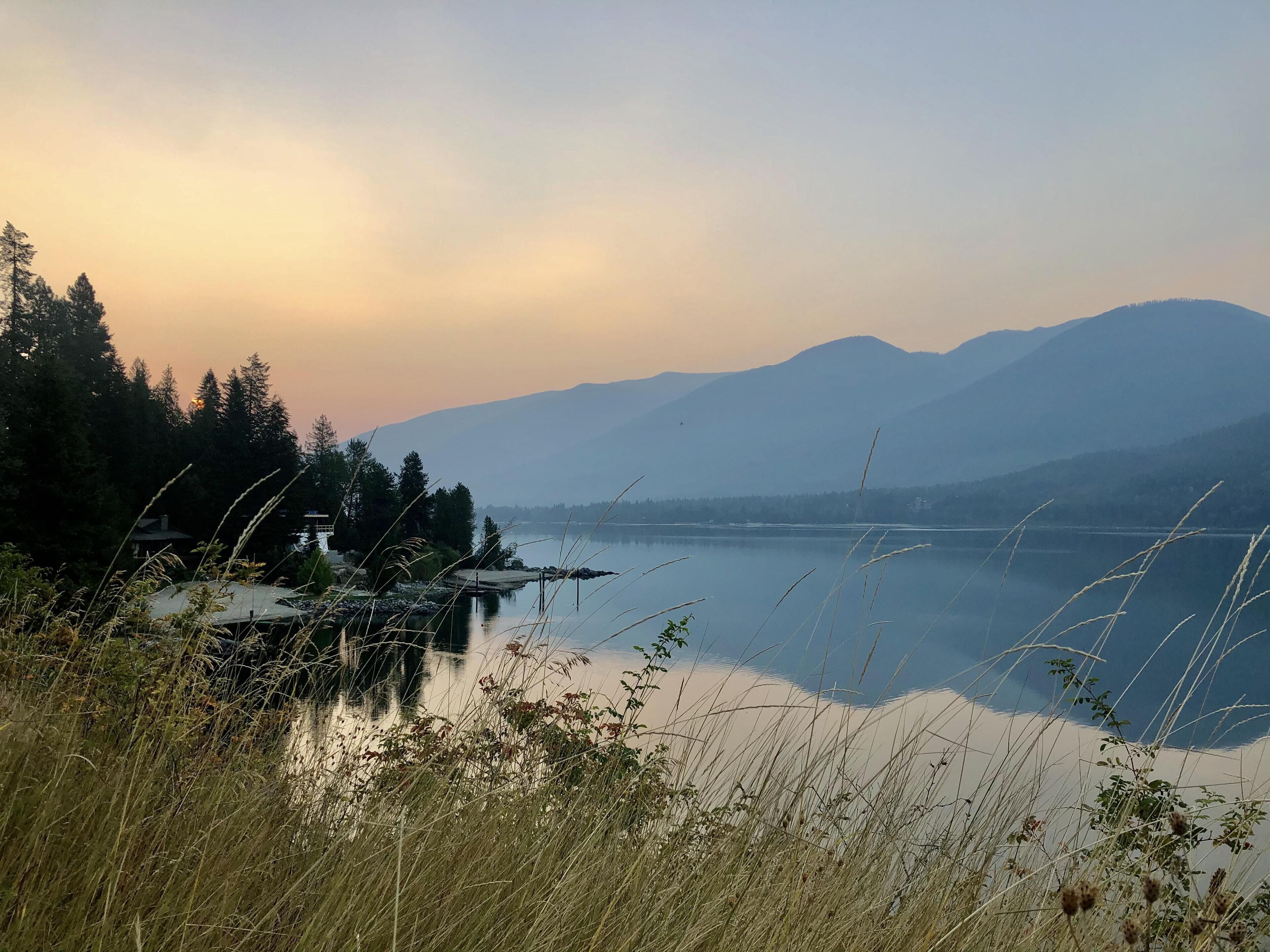 A serene lakeside view with mountains in the background and a dock extending into the water.