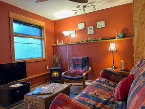 A cozy living room with a fireplace, a comfortable sofa, a television, and a bookshelf. - Downtown 1BR suite, ground floor, level entry. (Nelson)