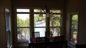 A dining area with a table and chairs, large windows with a view of trees and a body of water, and a chandelier. - “A Shore Thing “ A Gorgeous Lakefront Home Steps Away From Beaver Lake (Garfield)