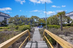 A wooden boardwalk leading to a building complex with multiple floors and a clear sky.