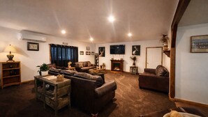 Uma sala de estar aconchegante com sofás de couro, lareira, televisão e estante de livros.